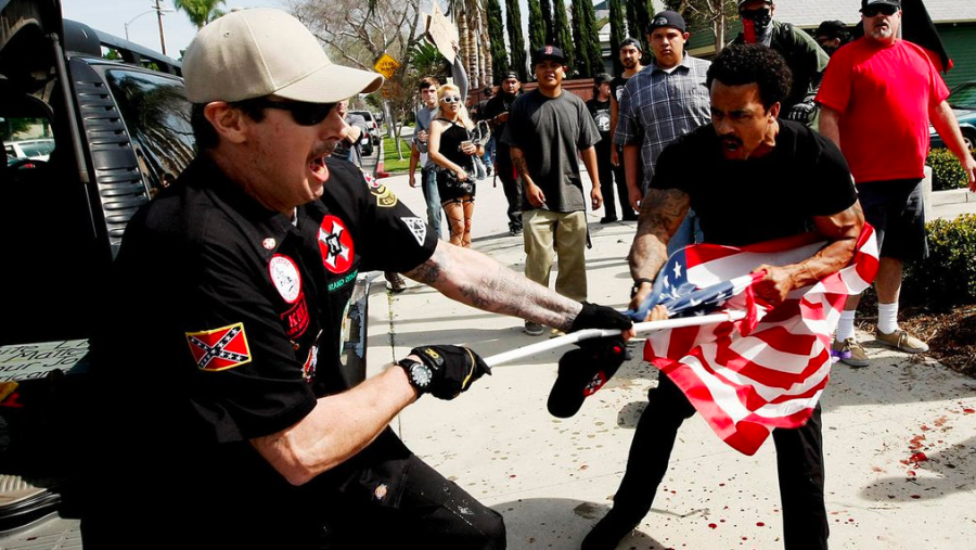 A Ku Klux Klansman, left, struggles with a protester for an American flag after members of the KKK tried to start a "White Lives Matter" rally at Pearson Park in Anaheim on Feb. 27, 2016. Three people were treated at the scene for stab wounds, and 13 people were arrested. (Credit: Luis Sinco / Los Angeles Times)