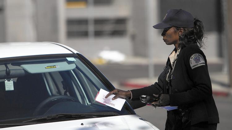 A parking enforcement officer tickets a car parked in an area scheduled for street sweeping in an undated photo. (Gina Ferazzi / Los Angeles Times)