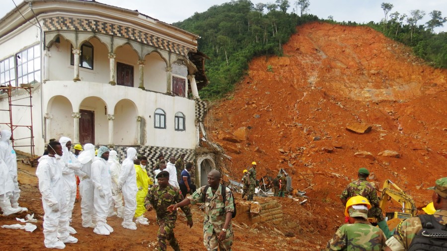 Search and rescue team members and soldiers operate near a mudslide site and damaged building near Freetown on August 15, 2017, after landslides struck the capital of the west African state of Sierra Leone. (Credit: SAIDU BAH/AFP/Getty Images)