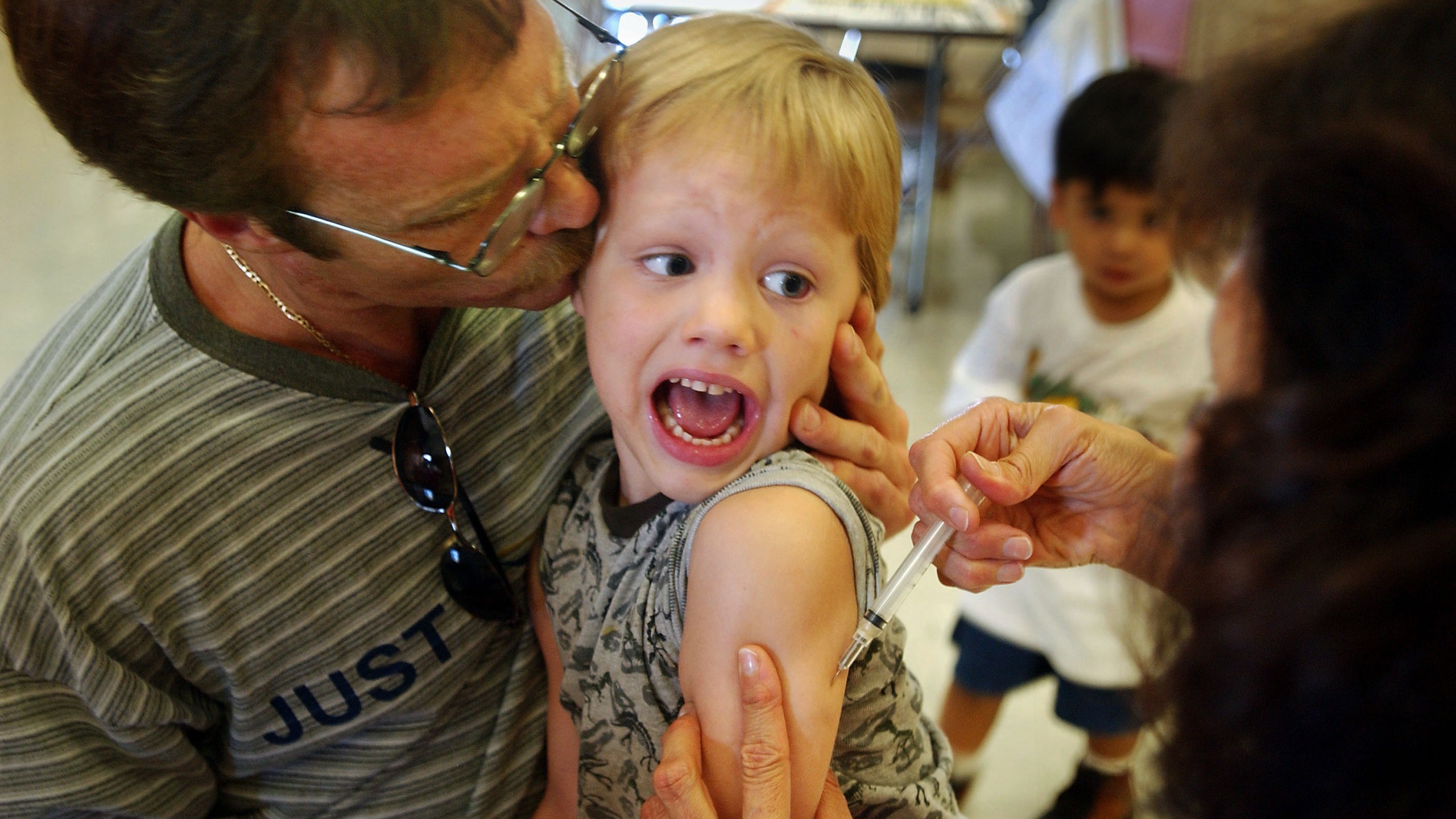 Incoming kindergartener Jeremy Conner, 5, reacts to a measles, mumps and rubella vaccination (MMR) as his father Mark Conner tries to comfort him Aug. 26, 2002, in Santa Ana. (Credit: David McNew/Getty Images)