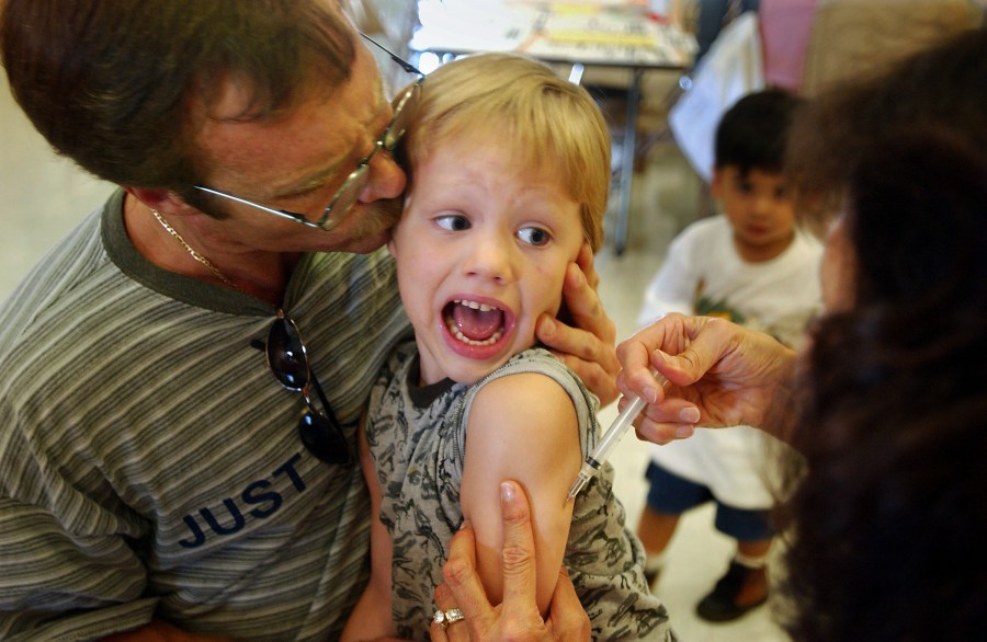 Incoming kindergartener Jeremy Conner, 5, reacts to a measles, mumps and rubella vaccination (MMR) as his father Mark Conner tries to comfort him Aug. 26, 2002, in Santa Ana. (Credit: David McNew/Getty Images)