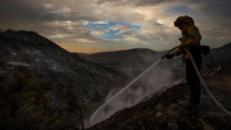 A firefighter is seen blowing water in a burned area. (Allen J. Schabern / Los Angeles Times)