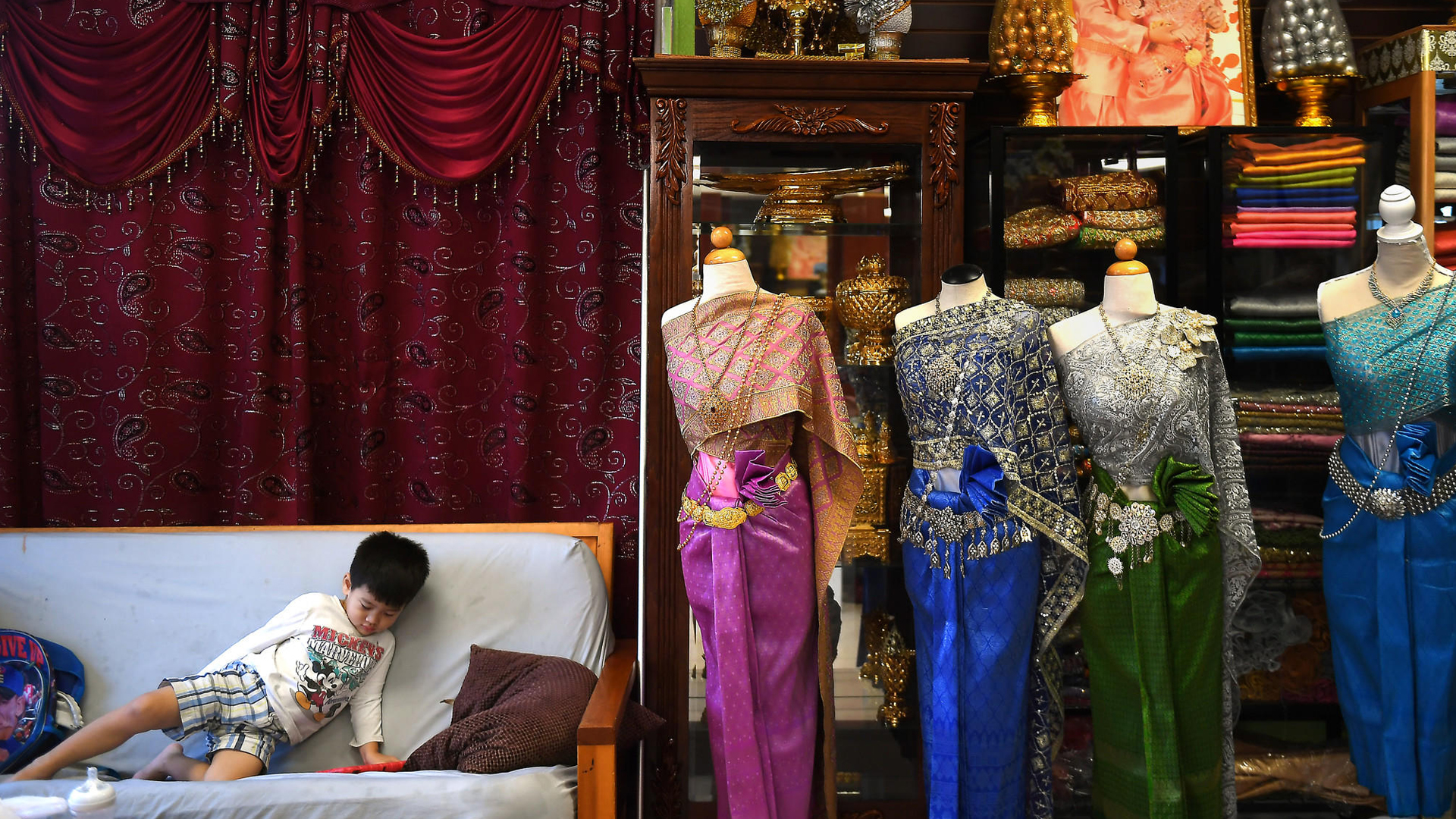 A boy sits near traditional Cambodian clothing at a shop in Long Beach's Cambodia Town. (Credit: Christina House/ Los Angeles Times)