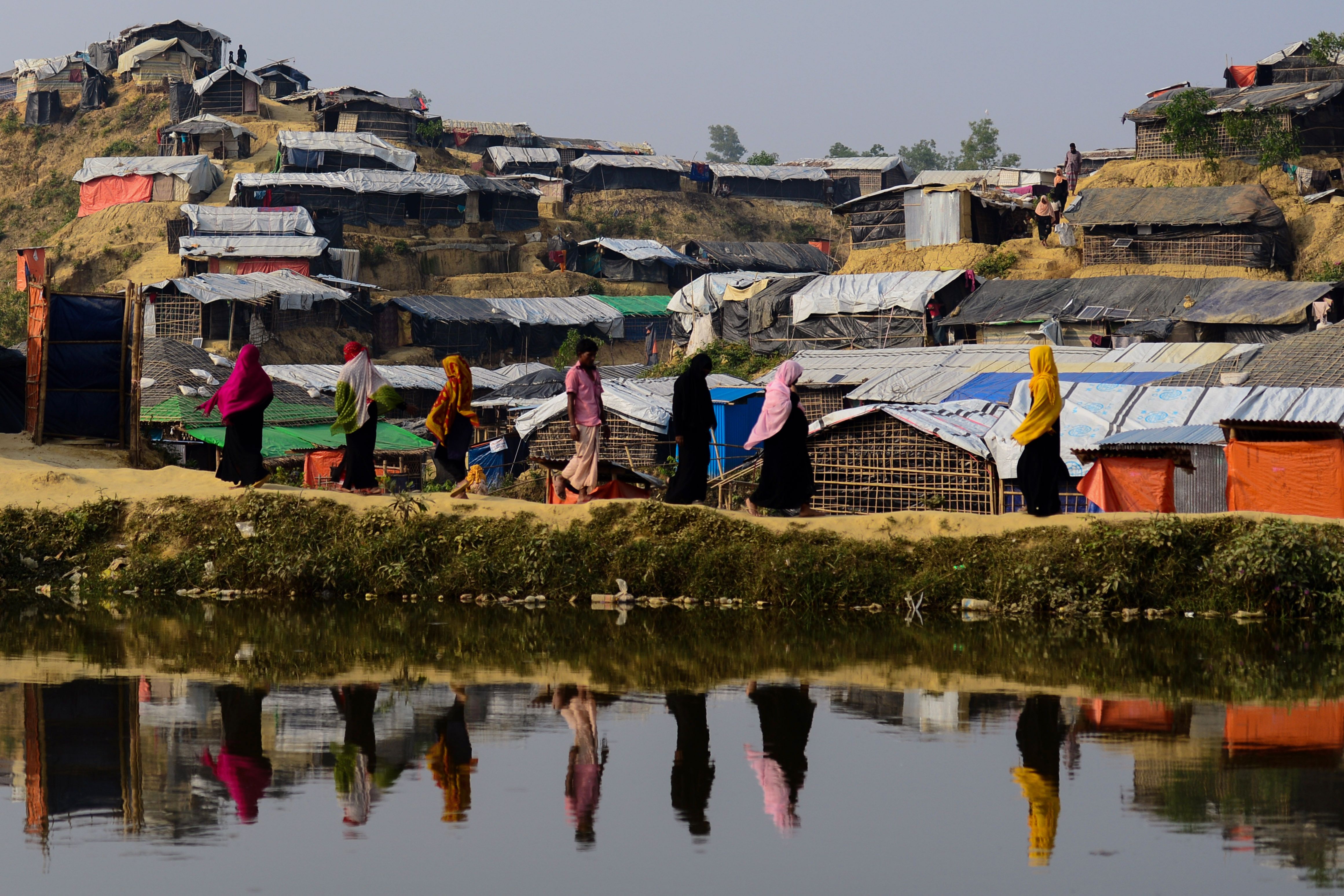 Rohingya refugees are reflected on a pond as they walk back to their homes at Balukhali refugee camp in the Bangladeshi district of Ukhia on Nov. 22, 2017. (Credit: Munir Uz Zaman / AFP / Getty Images)