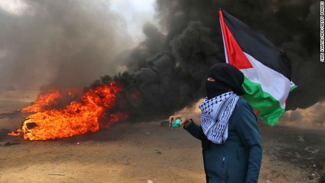 A Palestinian man holding his national flag walks in the smoke billowing from burning tires during clashes with Israeli forces along the border with the Gaza strip east of Khan Yunis on May 14, 2018. (Credit: SAID KHATIB/AFP/Getty Images)