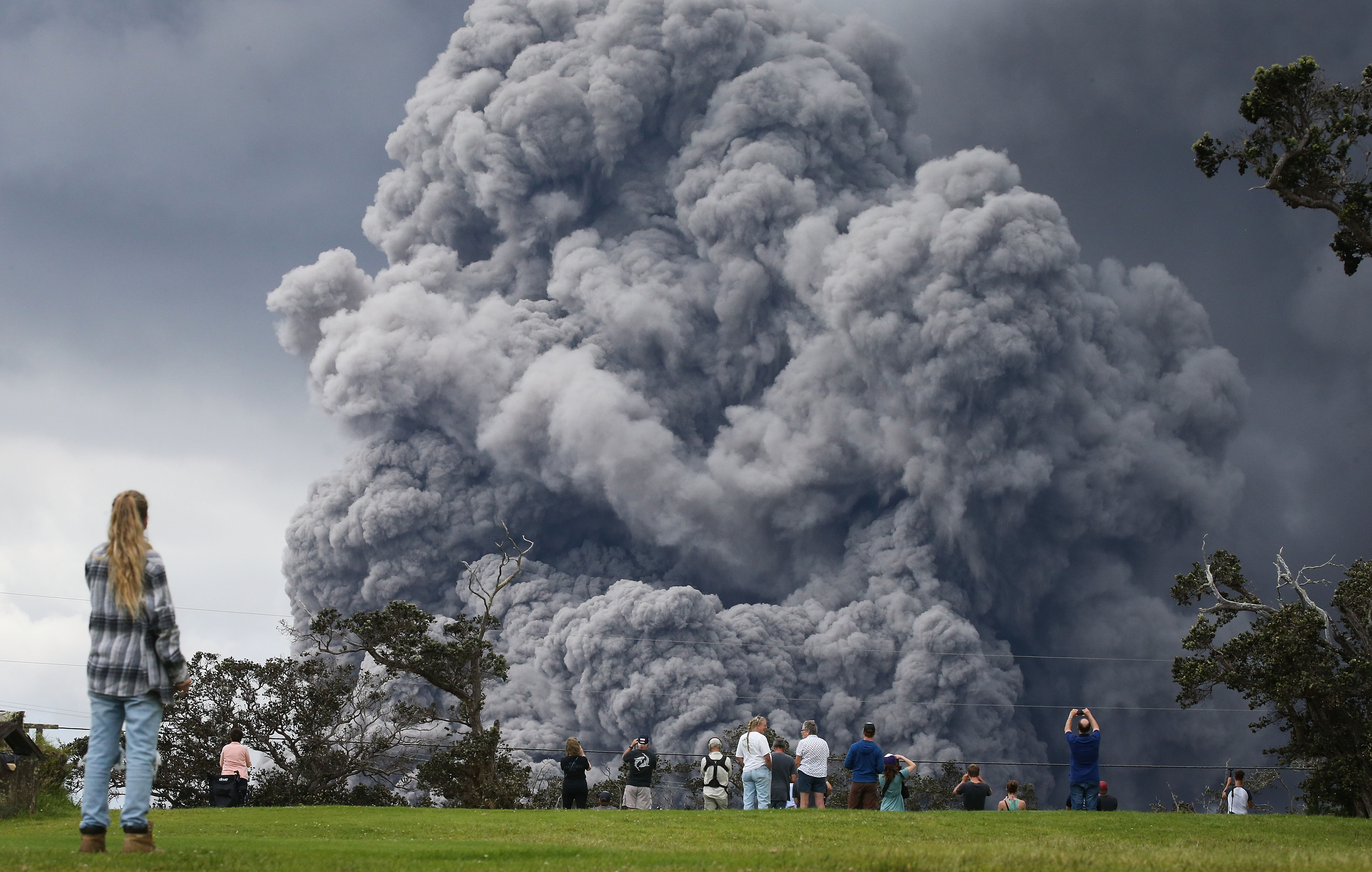 People watch at a golf course as an ash plume rises in the distance from the Kilauea volcano on Hawaii's Big Island on May 15, 2018 in Hawaii Volcanoes National Park, Hawaii. (Credit: Mario Tama/Getty Images)