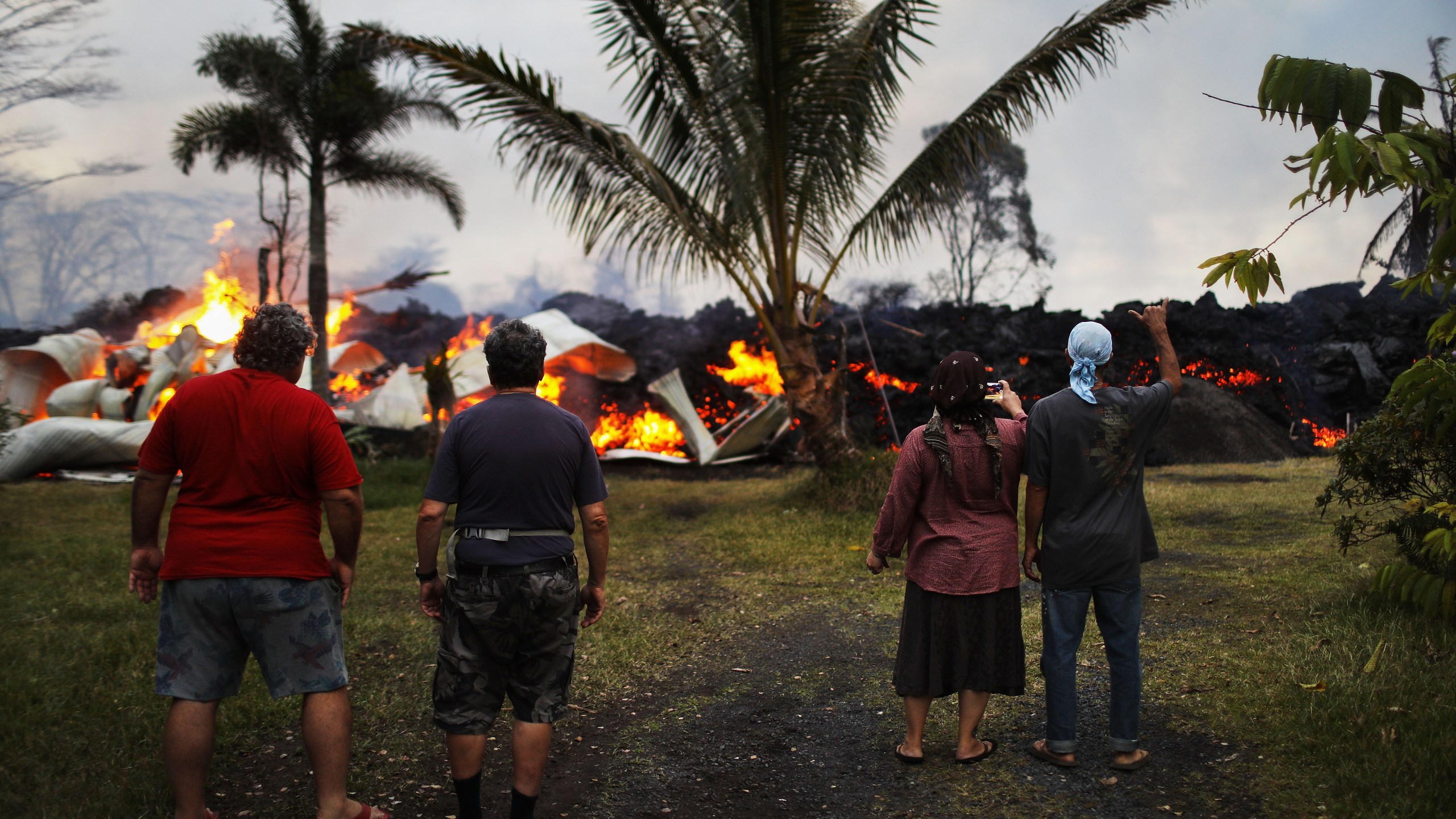 Community members watch as a home is destroyed by lava from a Kilauea volcano fissure in Leilani Estates, on Hawaii's Big Island, on May 25, 2018 in Pahoa, Hawaii. (Credit: Mario Tama/Getty Images)