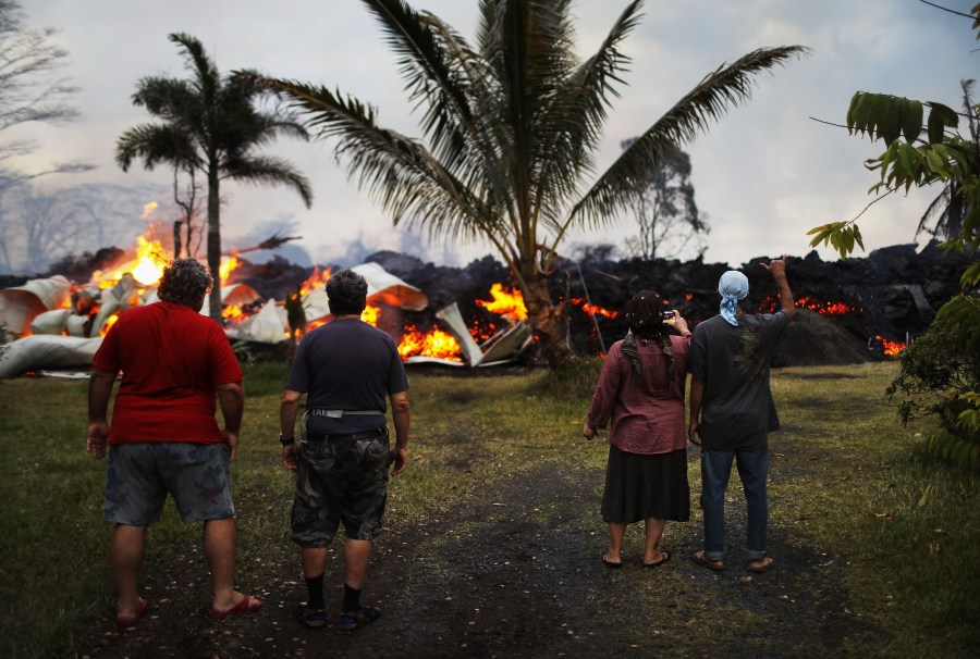 Community members watch as a home is destroyed by lava from a Kilauea volcano fissure in Leilani Estates, on Hawaii's Big Island, on May 25, 2018 in Pahoa, Hawaii. (Credit: Mario Tama/Getty Images)