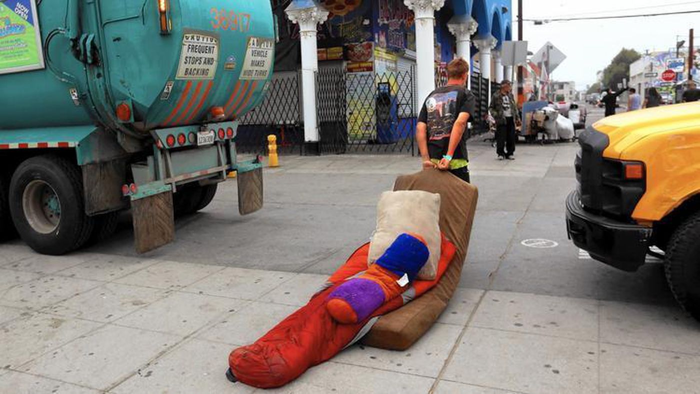 Marcus Steinlechner drags his bedding between a garbage truck and a city sanitation truck during a sweep of homeless encampments on the boardwalk at Venice Beach on June 26, 2015. (Credit: Los Angeles Times)