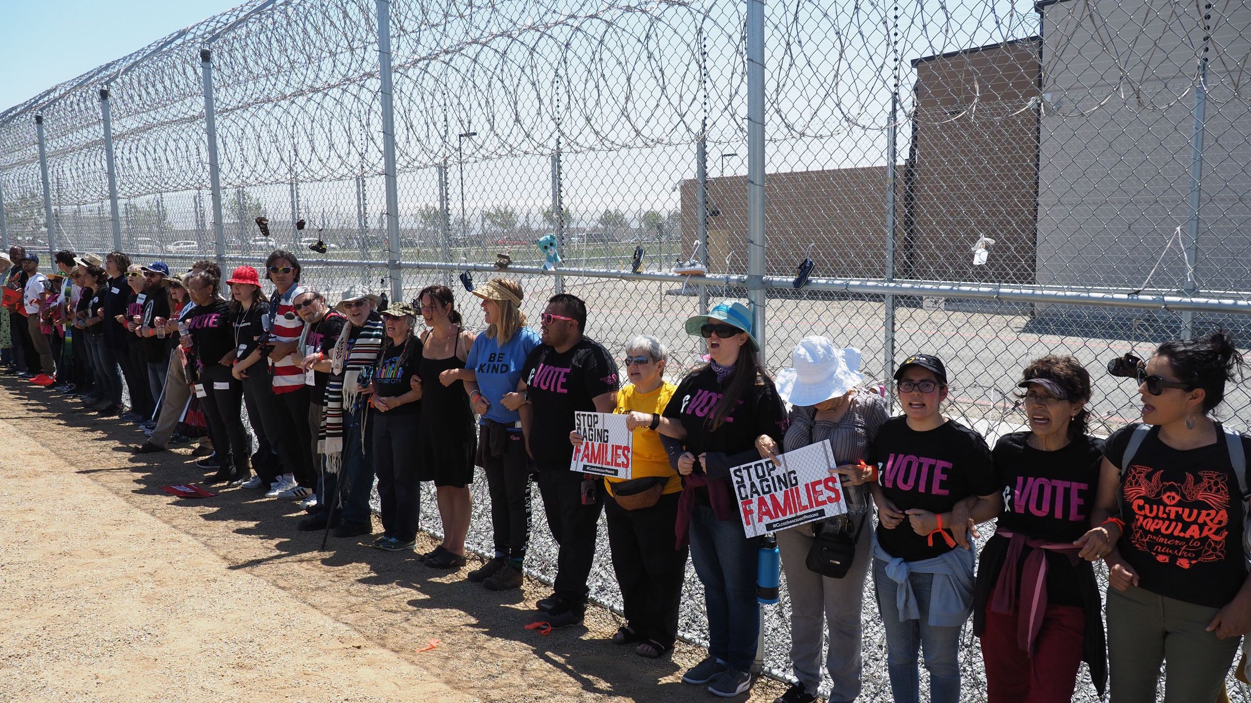 Protestors link arms after tying children's shoes and keys on the fence outside the Otay Mesa Detention Center during a demonstration against a Trump administration policy that separated migrant children from parents, in San Diego on June 23, 2018. (Credit: Robyn Beck / AFP / Getty Images)