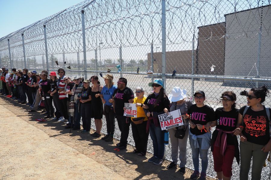 Protestors link arms after tying children's shoes and keys on the fence outside the Otay Mesa Detention Center during a demonstration against a Trump administration policy that separated migrant children from parents, in San Diego on June 23, 2018. (Credit: Robyn Beck / AFP / Getty Images)