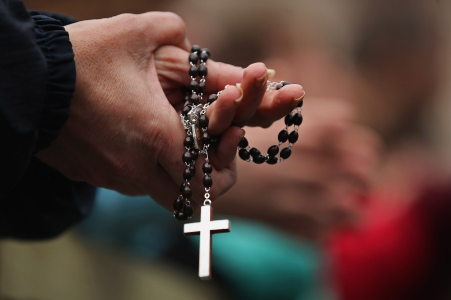 A woman holds rosary beads while she prays and waits for smoke to emanate from the chimney on the roof of the Sistine Chapel on March 13, 2013, in Vatican City. (Credit: Dan Kitwood / Getty Images)