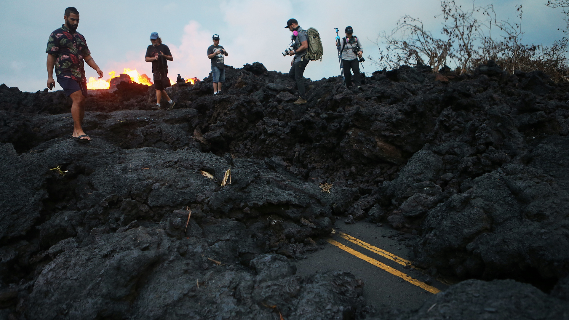 Onlookers and photographers walk on hardened lava from a Kilauea volcano fissure as lava erupts in Leilani Estates, on Hawaii's Big Island, on May 26, 2018. (Credit: Mario Tama/Getty Images)