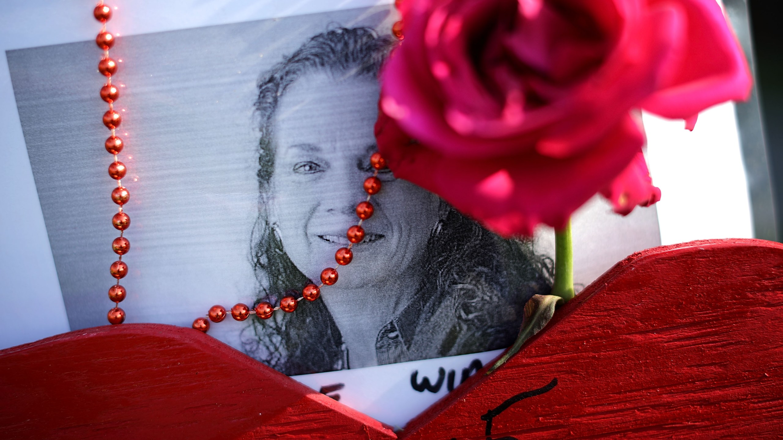 Beads, a wooden heart and flowers decorate a photograph of Wendi Winters at a makeshift memorial outside the Capitol Gazette offices July 2, 2018, in Annapolis, Md. Winters, 65, a local news reporter and community columnist, was killed in the shooting along with her colleagues, Gerald Fischman, 61, an editorial editor; Rob Hiaasen, 59, an editor and columnist; John McNamara, 56, a sports reporter and editor; and Rebecca Smith, 34, a sales assistant. (Credit: Chip Somodevilla/Getty Images)