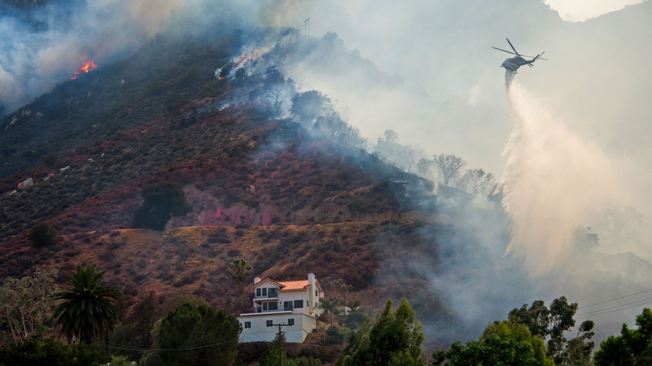 A helicopter drops water to protect a home from the Holy Fire in Lake Elsinore, California on Aug. 10, 2018.(Credit: ROBYN BECK/AFP/Getty Images)