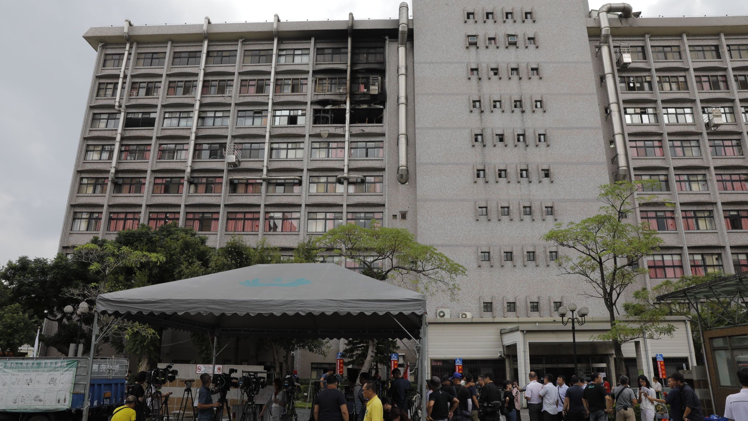 Members of the media gather outside as burnt out windows (top) are seen on a hospital following a fire on the seventh floor in New Taipei City on August 13, 2018. (Credit: Daniel Shih/AFP/Getty Images)