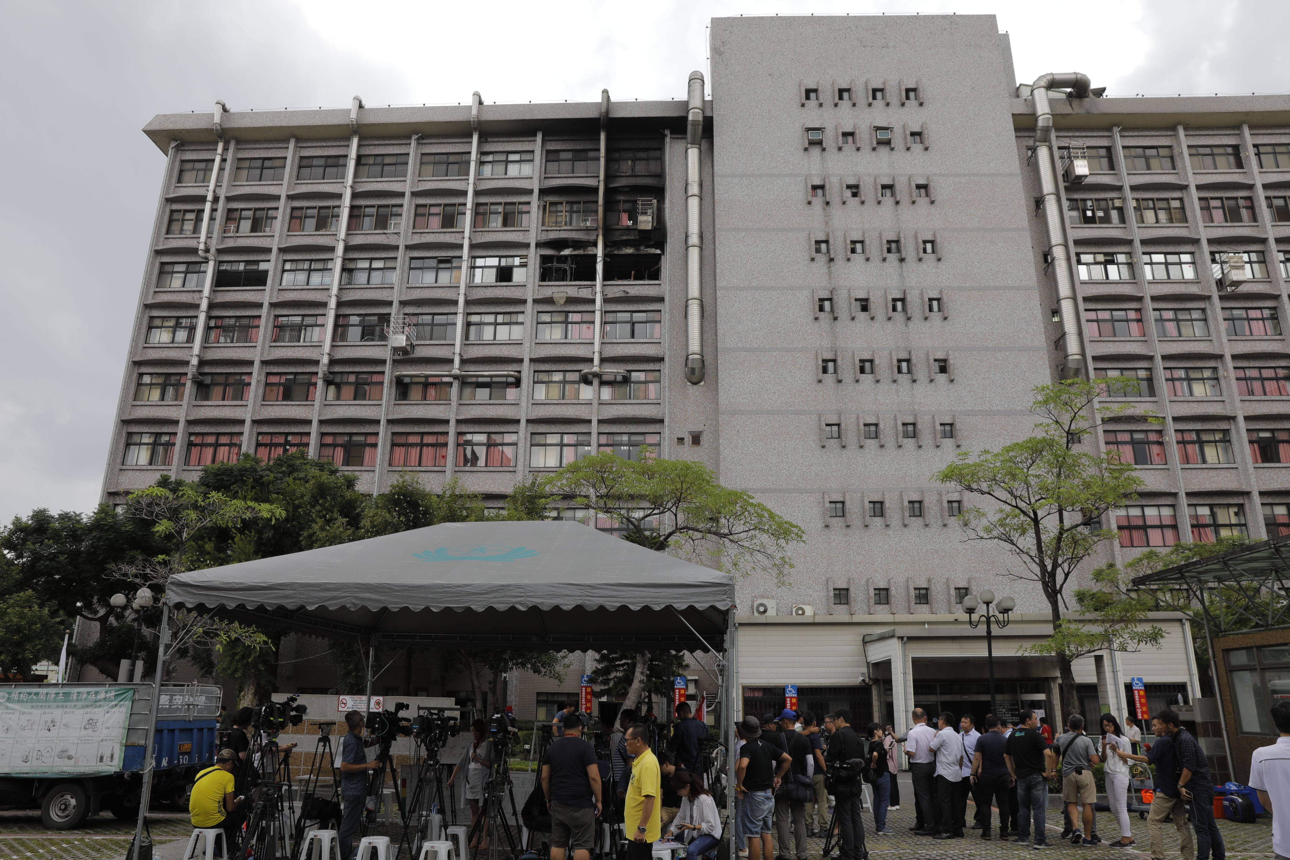 Members of the media gather outside as burnt out windows (top) are seen on a hospital following a fire on the seventh floor in New Taipei City on August 13, 2018. (Credit: Daniel Shih/AFP/Getty Images)