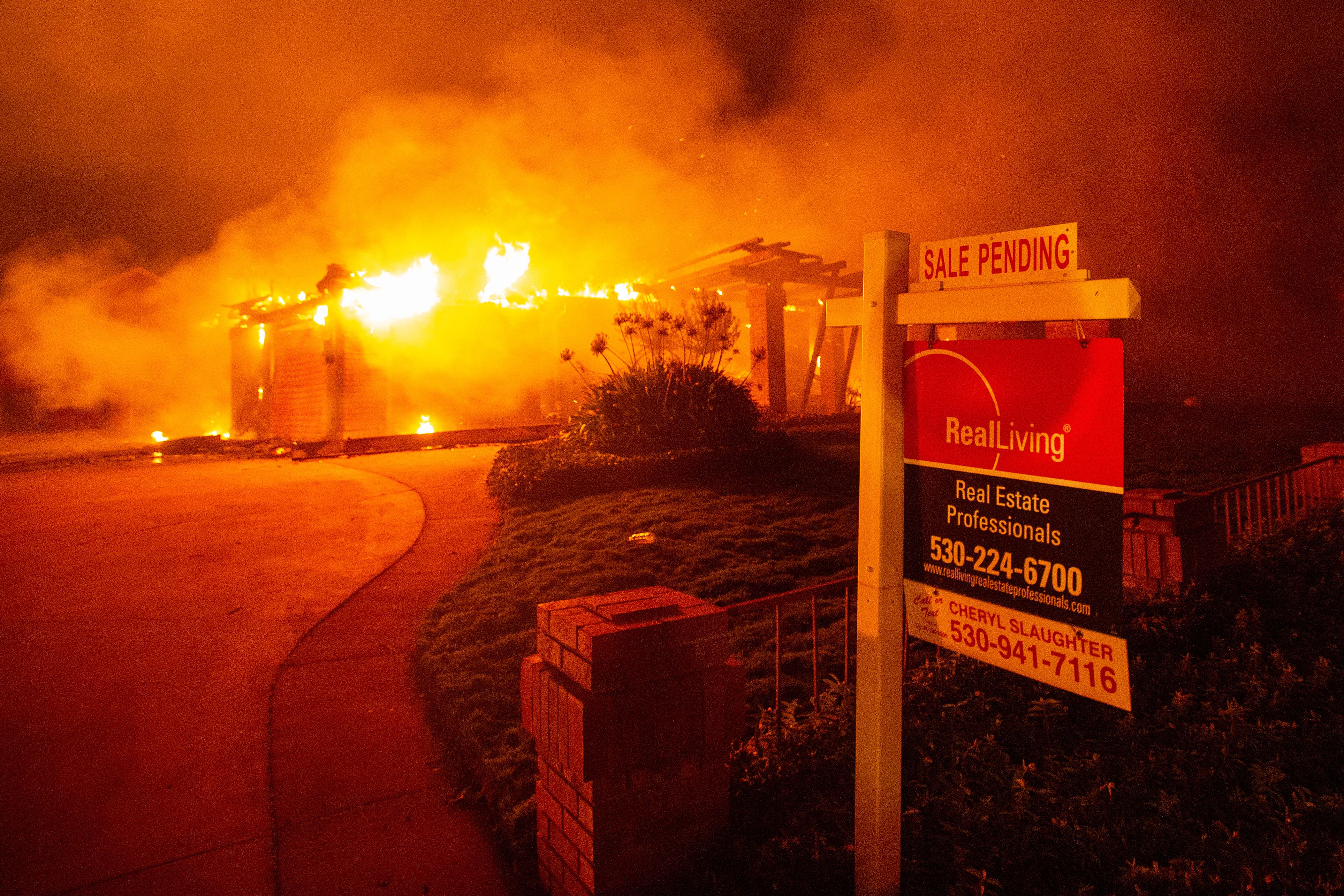 A real estate sign is seen in front of a burning home in Redding during the Carr Fire on July 27, 2018. (Credit: Josh Edelson / AFP / Getty Images)