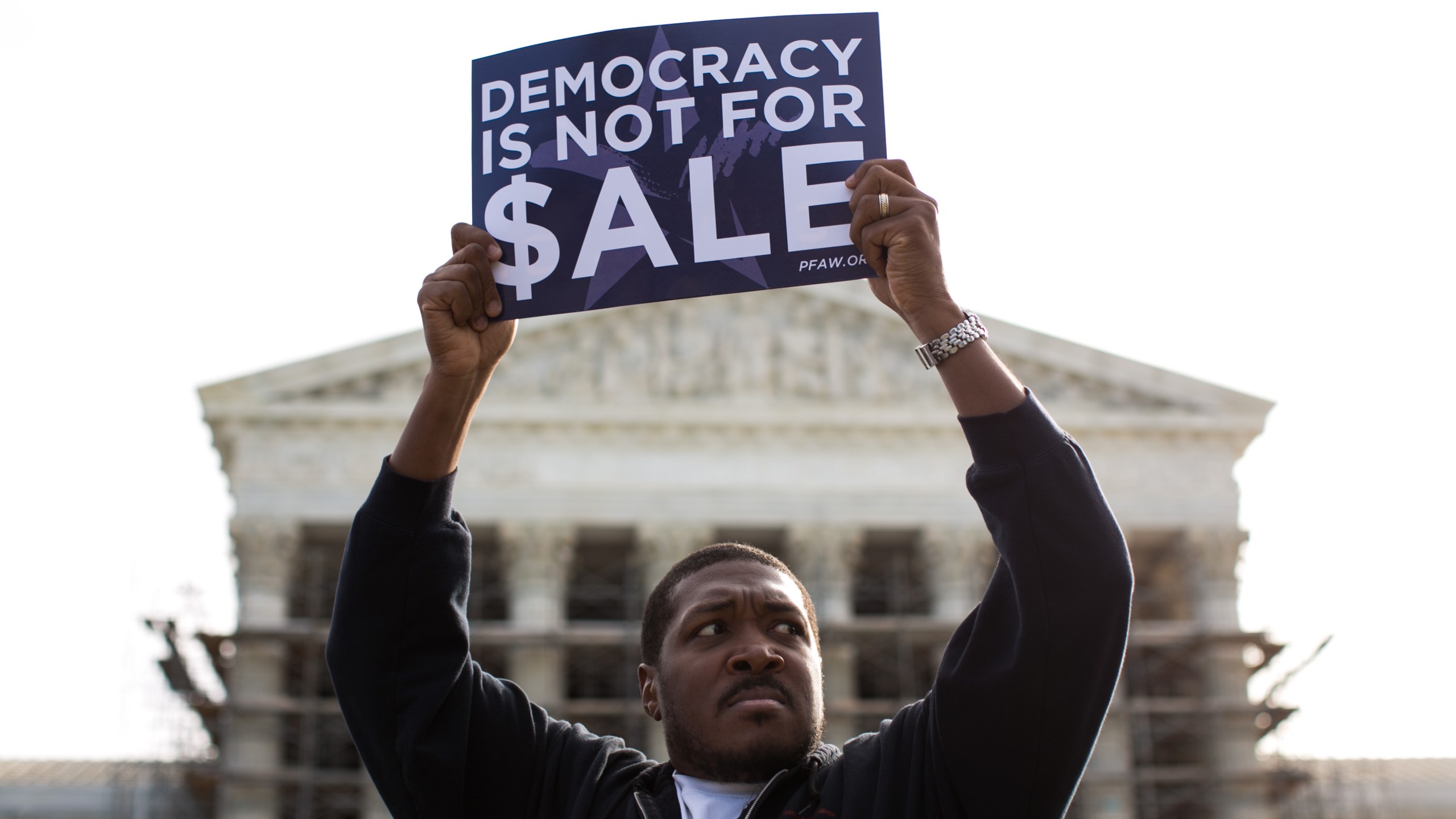 Cornell Woolridge holds a sign as he rallies against money in politics at the Supreme Court in Washington, D.C. on Oct. 8, 2013. (Credit: Drew Angerer/Getty Images)