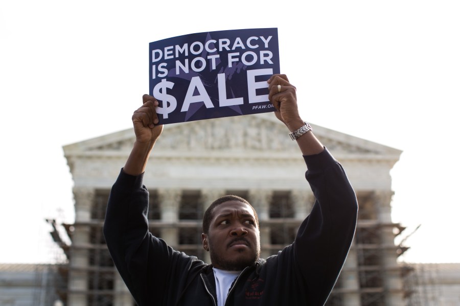 Cornell Woolridge holds a sign as he rallies against money in politics at the Supreme Court in Washington, D.C. on Oct. 8, 2013. (Credit: Drew Angerer/Getty Images)