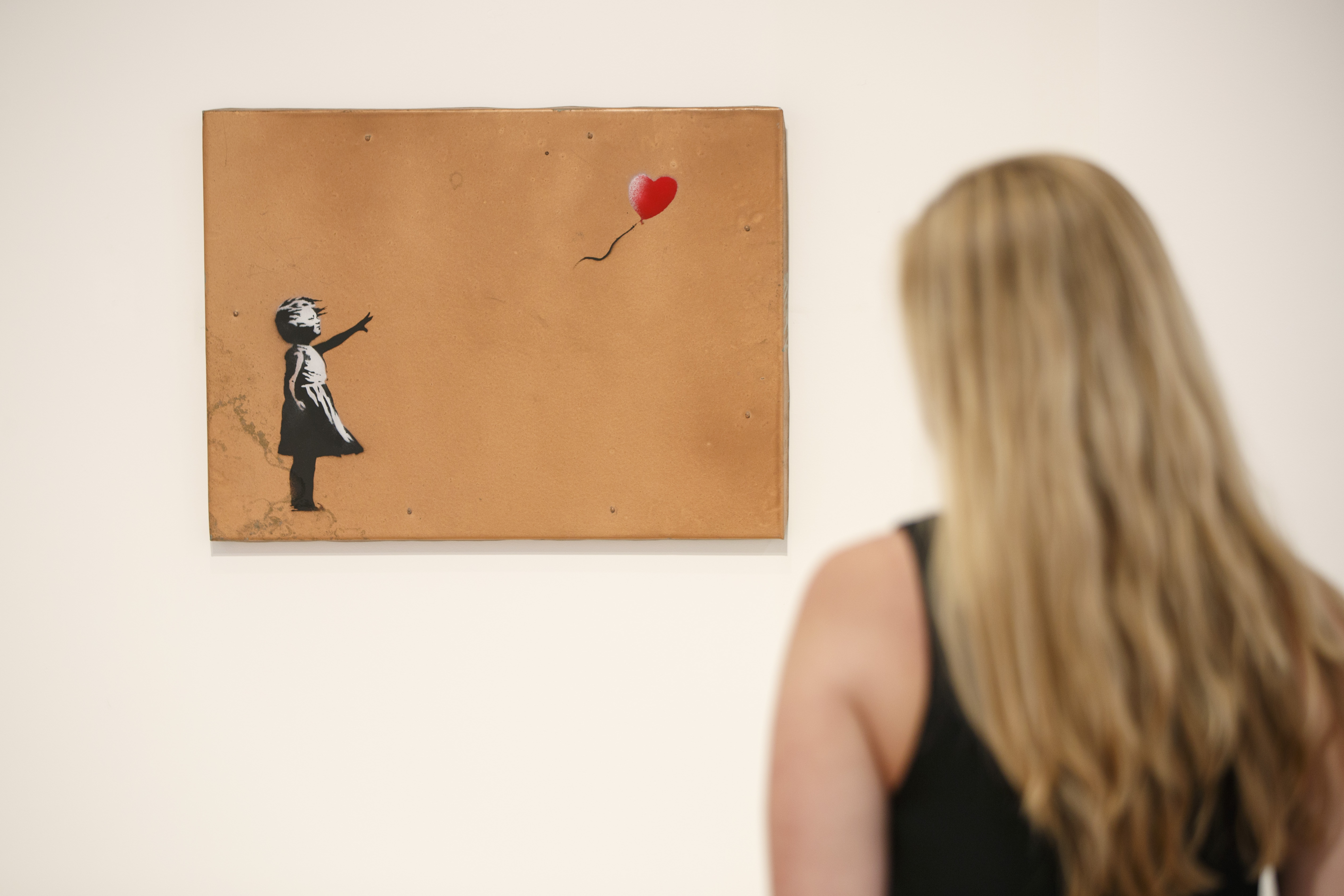 A gallery assistant poses with 'Girl with Balloon' 2006 artwork by Banksy at Lazinc Gallery in London on July 11, 2018. - The exhibition opens to the public on July 12, 2018. (Credit: TOLGA AKMEN/AFP/Getty Images)