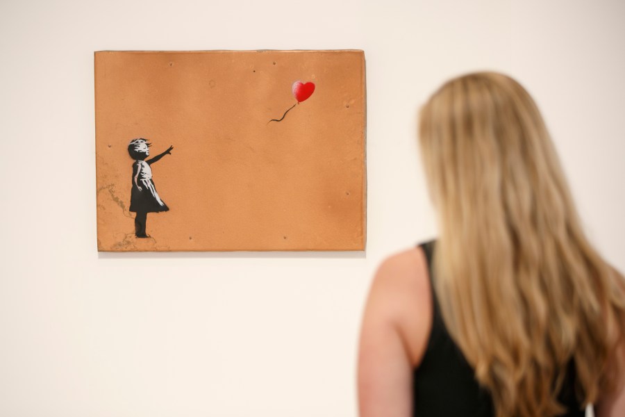 A gallery assistant poses with 'Girl with Balloon' 2006 artwork by Banksy at Lazinc Gallery in London on July 11, 2018. - The exhibition opens to the public on July 12, 2018. (Credit: TOLGA AKMEN/AFP/Getty Images)