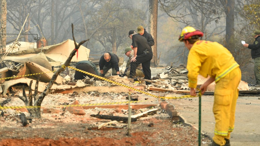 A CalFire firefighter sets up tape as Yuba and Butte County Sheriff officers recover a body at a burned out residence in Paradise on November 10, 2018. (Credit: JOSH EDELSON/AFP/Getty Images)