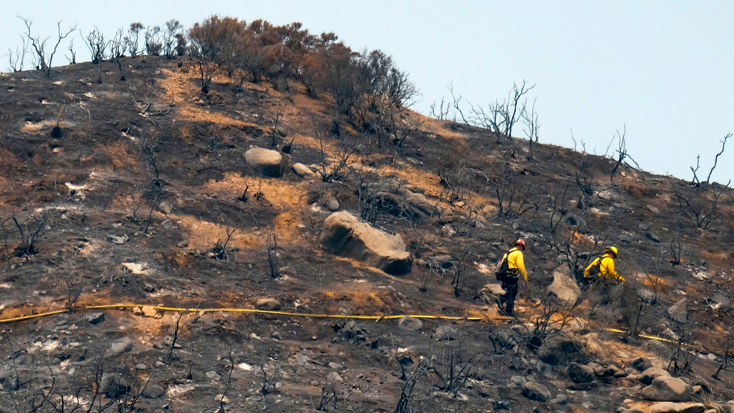 In this file photo taken on Aug. 10, 2018, firefighters walk through an area burned by the Holy Fire in Lake Elsinore. (Credit: Ringo Chiu / AFP / Getty Images)