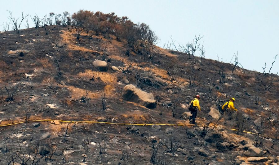 In this file photo taken on Aug. 10, 2018, firefighters walk through an area burned by the Holy Fire in Lake Elsinore. (Credit: Ringo Chiu / AFP / Getty Images)