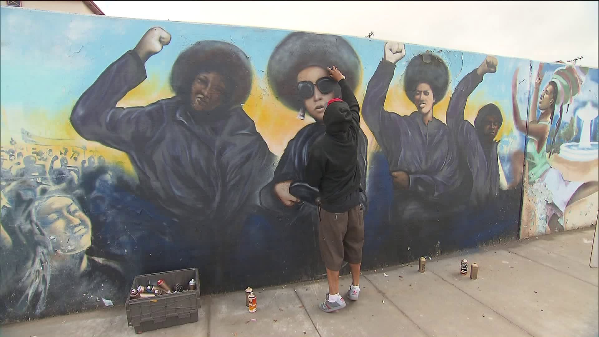 Artist Enkone works to cover up swastikas painted on the "Our Mighty Contribution" mural at Crenshaw Boulevard and 50th Street in the Hyde Park neighborhood of Los Angeles on Nov. 29, 2018. (Credit: CNN)