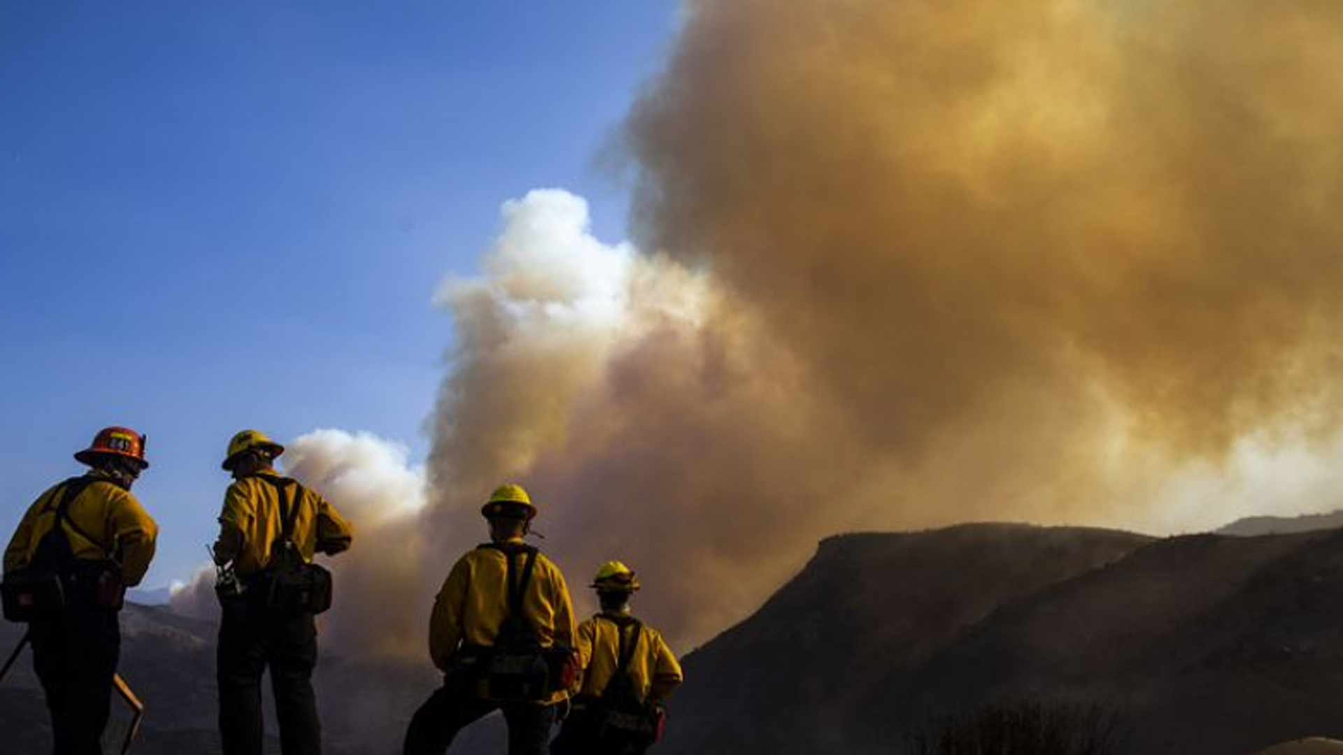 Firefighters work to put out hot spots in and around structures destroyed by the Woolsey fire as a plume of smoke rises from near the Chatsworth Reservoir in West Hills on Sunday. (Credit: Kent Nishimura / Los Angeles Times)