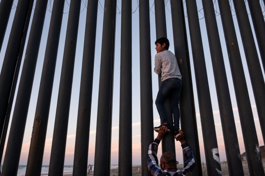 A man helps a boy to have a better look at the US-Mexico border wall in Playas de Tijuana, northwestern Mexico, November 18, 2018. (Credit: GUILLERMO ARIAS/AFP/Getty Images)