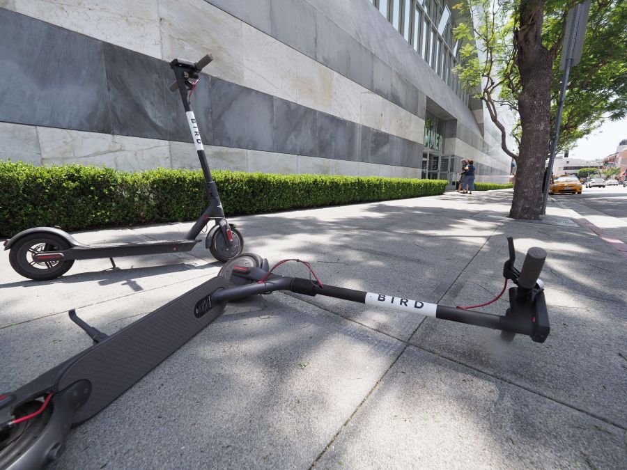 A pedestrian walks past two Bird dockless scooters, one laying on its side, in the middle of a sidewalk in Westwood on July 10, 2018. (Credit: ROBYN BECK/AFP/Getty Images)