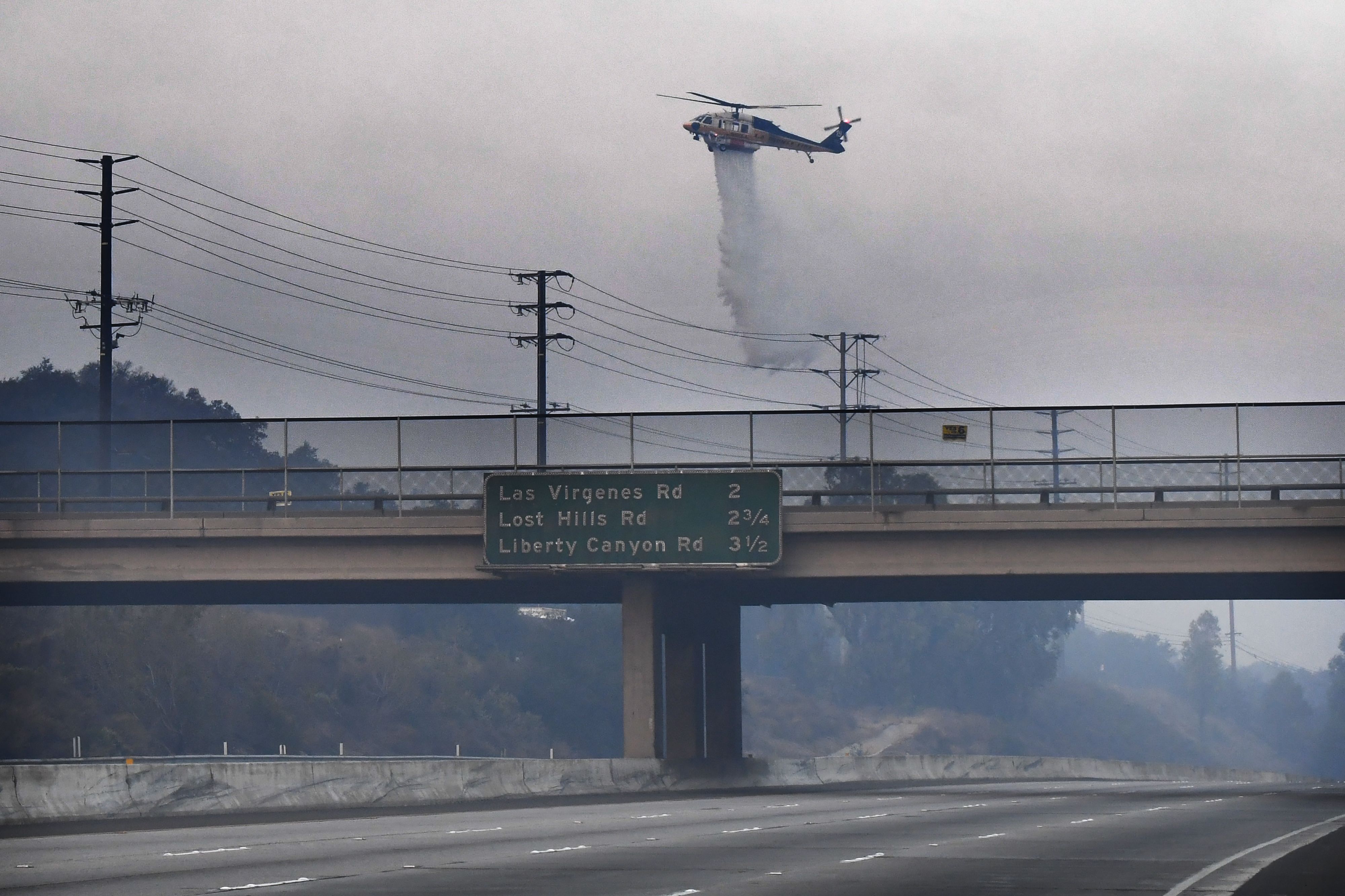 A helicopter drops water on a hot spot from the Woolsey Fire on Nov. 10, 2018 along the 101 Freeway in Calabasas. (Credit: ROBYN BECK/AFP/Getty Images)