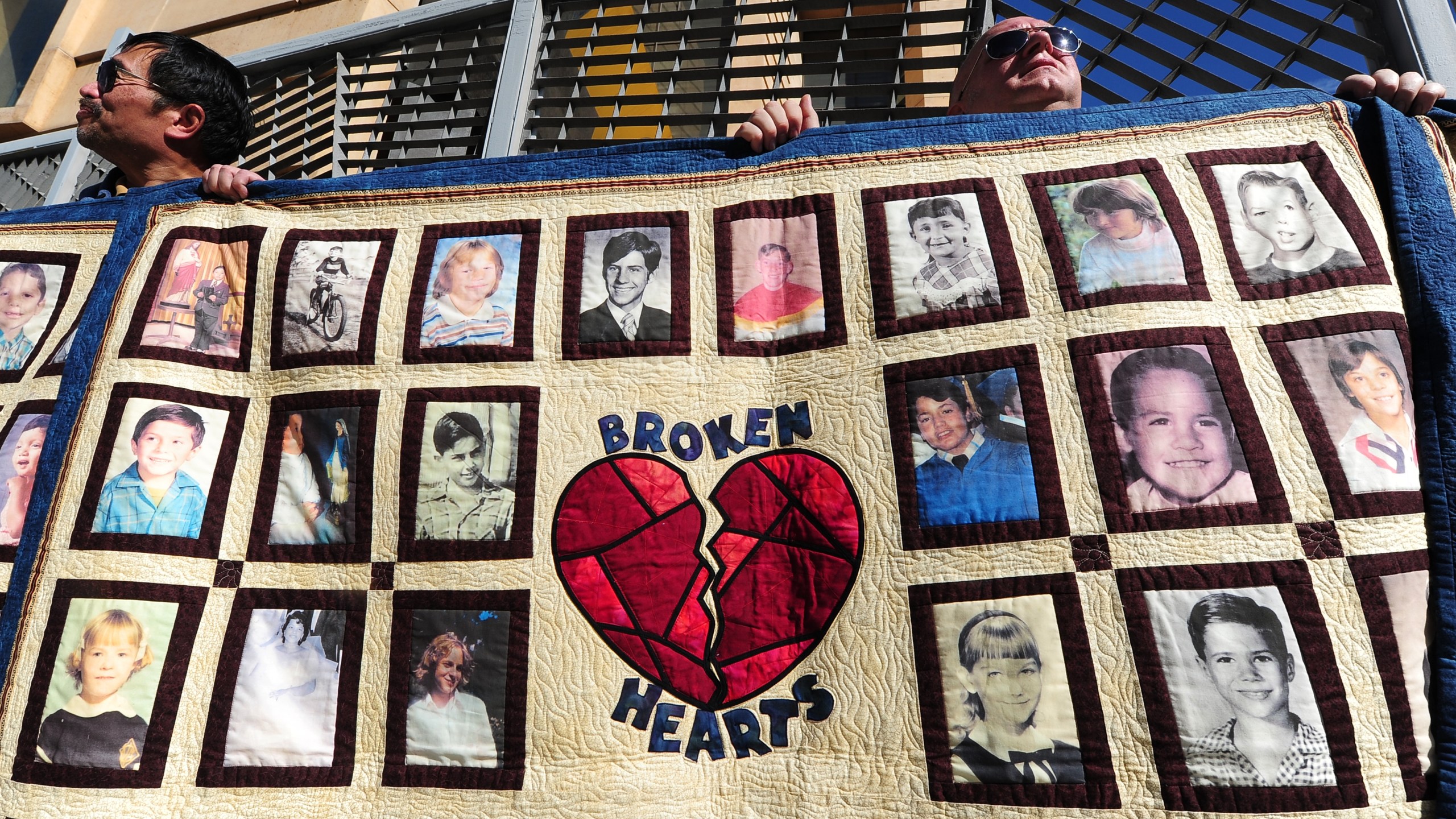 Abuse victim Jorgen Olsen, right, and supporter Glenn Gorospa, left, hold quilts bearing portraits of abused children while gathered outside the Cathedral of Our Lady of the Angels on Feb. 1, 2013. (Credit: Frederic J. Brown / AFP / Getty Images)