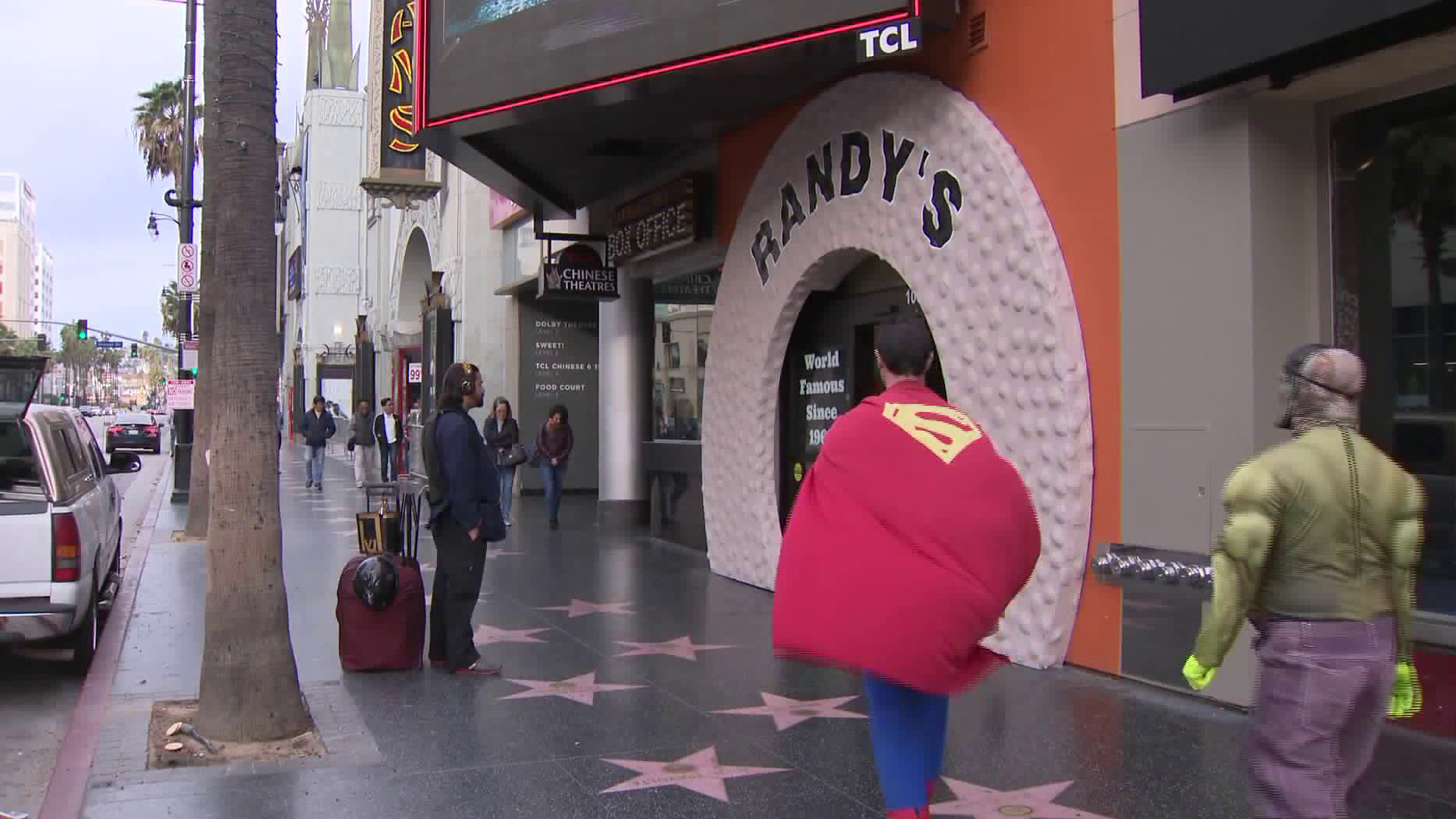 Two people dressed as Superman and the Hulk walk by Randy's Donuts in Hollywood on Dec. 10, 2018. (Credit: KTLA)