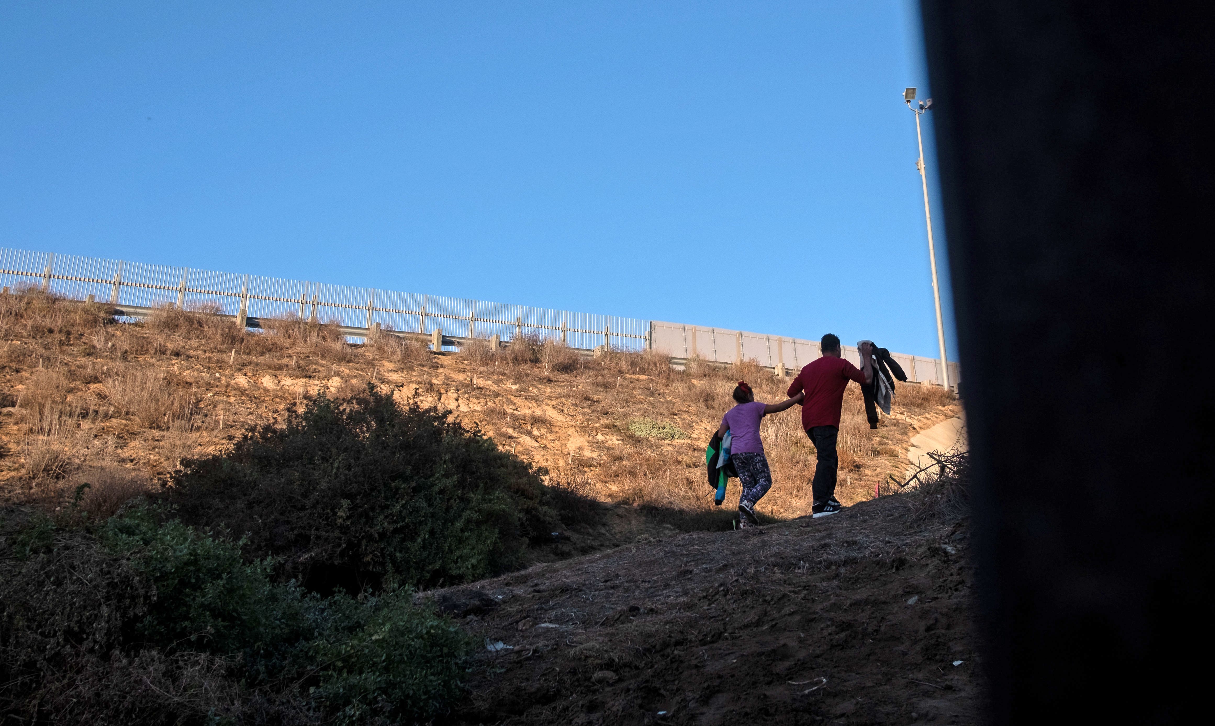 Honduran Andrea Nicolle, 10, and her father, Tony, traveling in a caravan of Central American migrants hoping to get to the United States, walk to surrender to the Border Patrol after crossing through a hole on the ground under the metal barrier separating Mexico and the U.S. on Dec. 4, 2018. (Credit: Guillermo Arias / AFP / Getty Images)