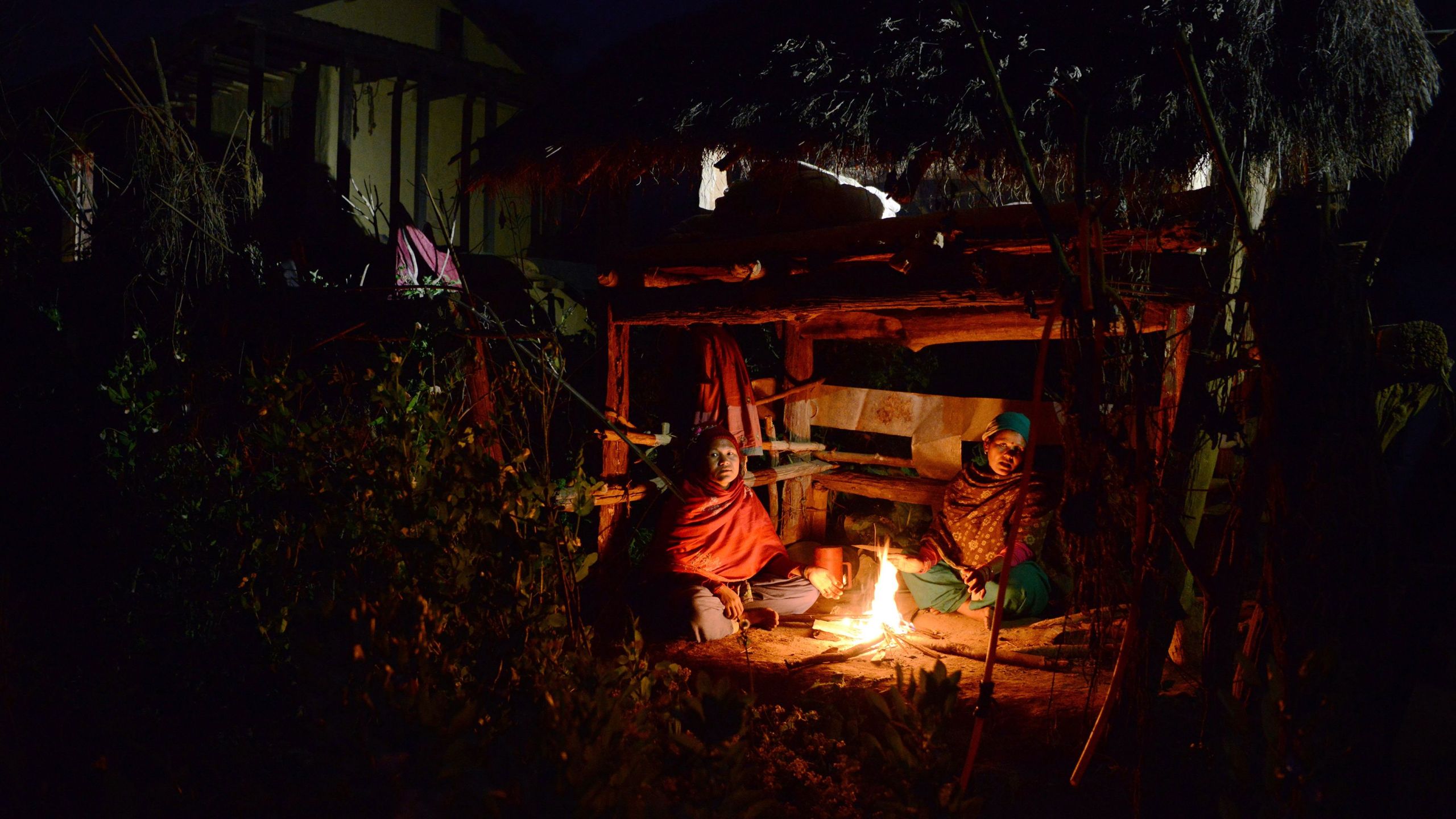 In this photograph taken on February 3, 2017, Nepalese women Pabitra Giri (L) and Yum Kumari Giri (R) sit by a fire as they live in a Chhaupadi hut during their menstruation period in Surkhet District, some 520km west of Kathmandu. The practice of banning women from the home when they are menstruating is linked to Hinduism and considers women untouchable at this time. They are banished from the home -- barred from touching food, religious icons, cattle and men -- and forced into a monthly exile sleeping in basic huts. (Credit: PRAKASH MATHEMA/AFP/Getty Images)