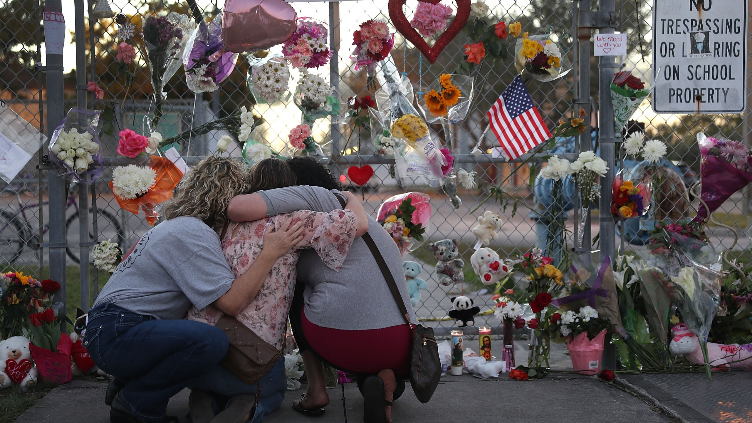 Shari Unger, Melissa Goldsmith and Giulianna Cerbono (from left) hug each other as they visit a makeshift memorial set up in front of Marjory Stoneman Douglas High School in Parkland, Florida, on Feb. 18, 2018. (Credit: Joe Raedle / Getty Images)