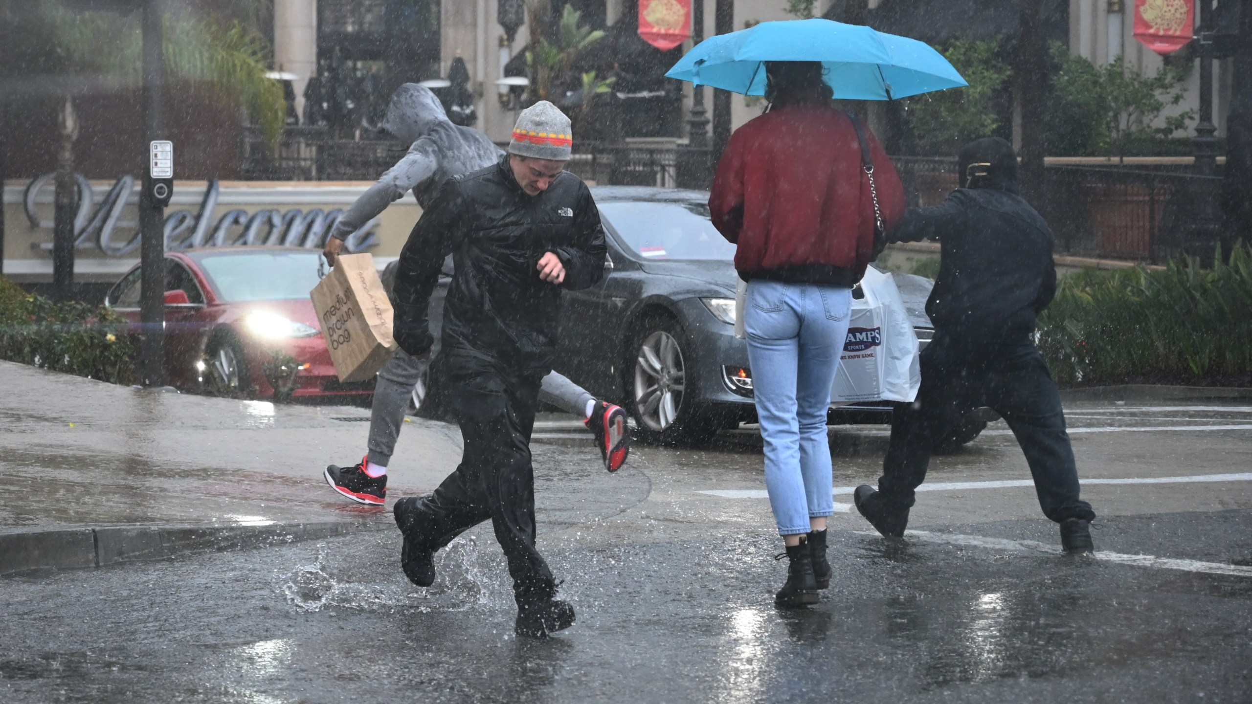 People run through water flooding a street in Glendale on Feb. 2, 2019. (Credit: ROBYN BECK/AFP/Getty Images)