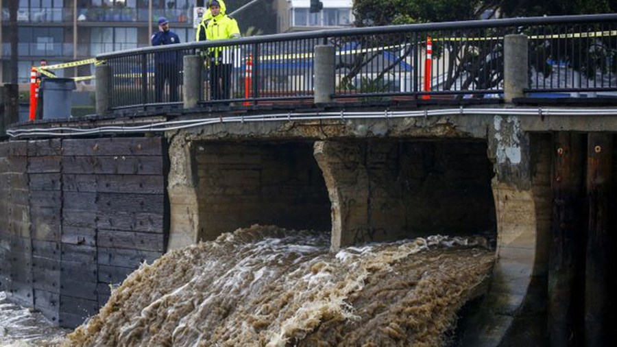 People walking along the Laguna Beach boardwalk look at stormwater pouring out to the ocean in Laguna Beach in an undated photo. (Credit: Kent Nishimura / Los Angeles Times)