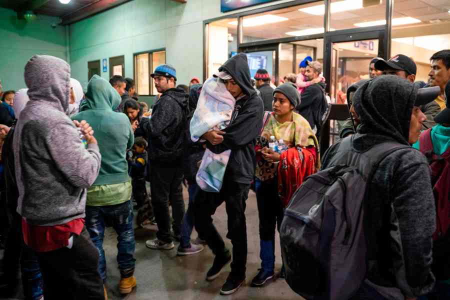 Asylum seekers stand at a bus stop after being dropped off by Immigration and Customs Enforcement at the Greyhound bus station in downtown El Paso, Texas late on Dec. 23, 2018. (Credit: PAUL RATJE/AFP/Getty Images)