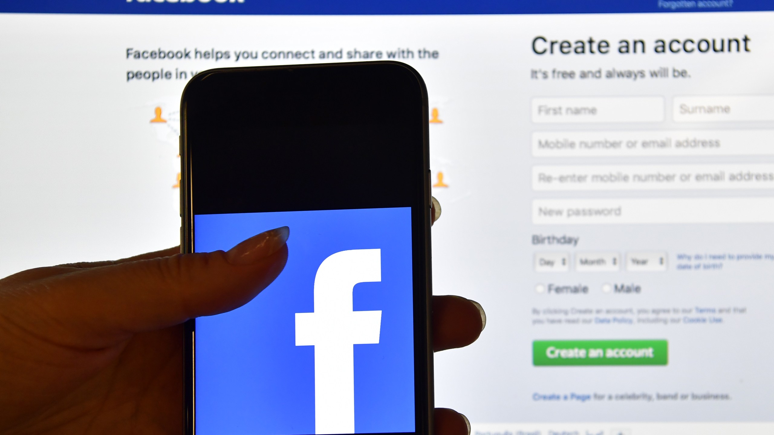 A person holds an iPhone displaying the Facebook app logo in front of a computer screen showing the Facebook login page on August 3, 2016 in London, England. (Credit: Carl Court/Getty Images)