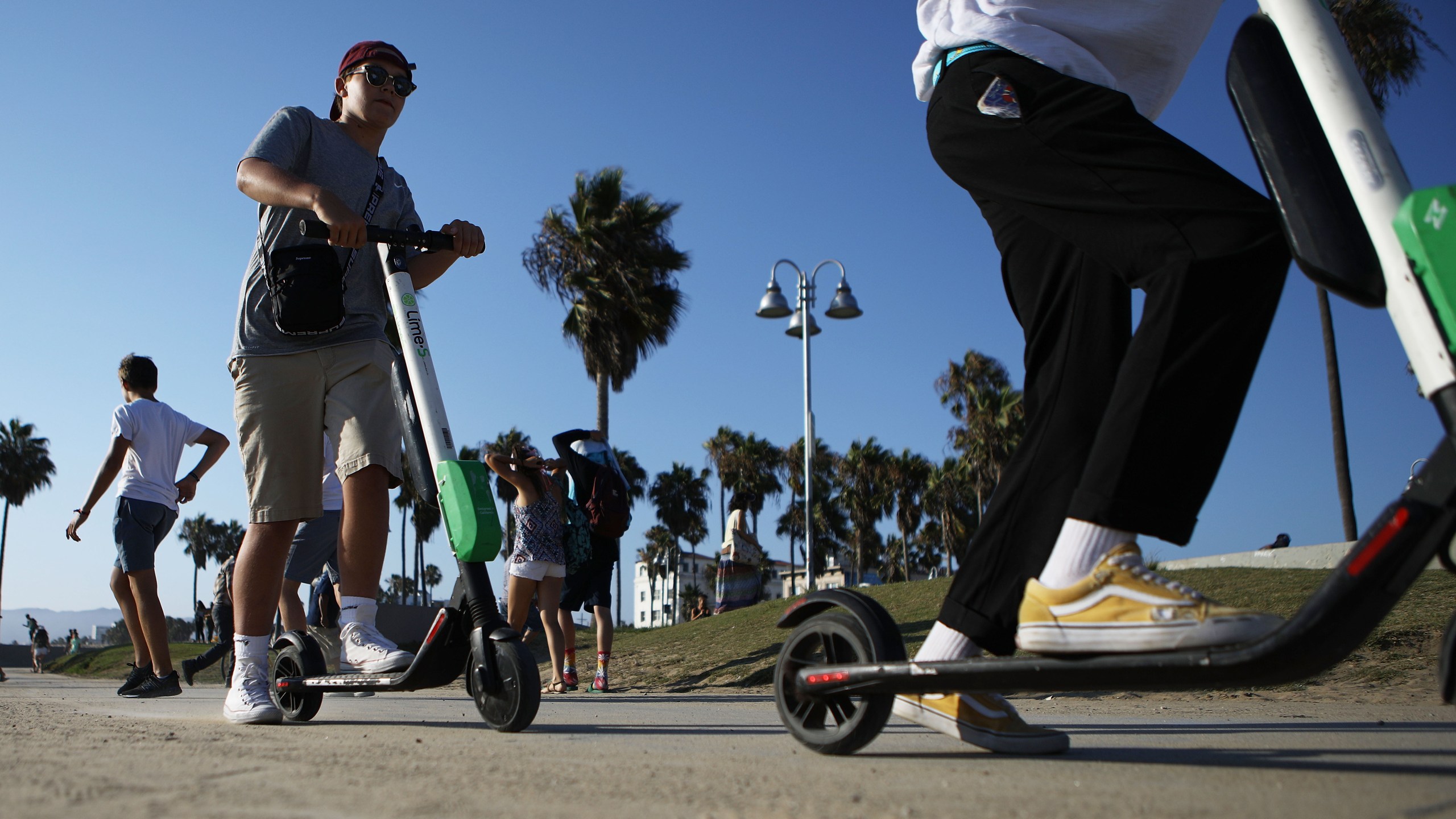 People ride Lime shared dockless electric scooters along Venice Beach on Aug. 13, 2018, in Los Angeles. (Credit: Mario Tama/Getty Images)