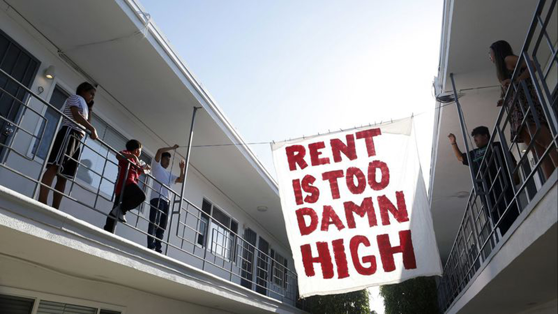 A 2019 file photo shows organizers with Housing Long Beach, a local advocacy group, hang up a sign in the courtyard of an apartment complex on Cedar Avenue in Long Beach. (Katie Falkenberg / Los Angeles Times)