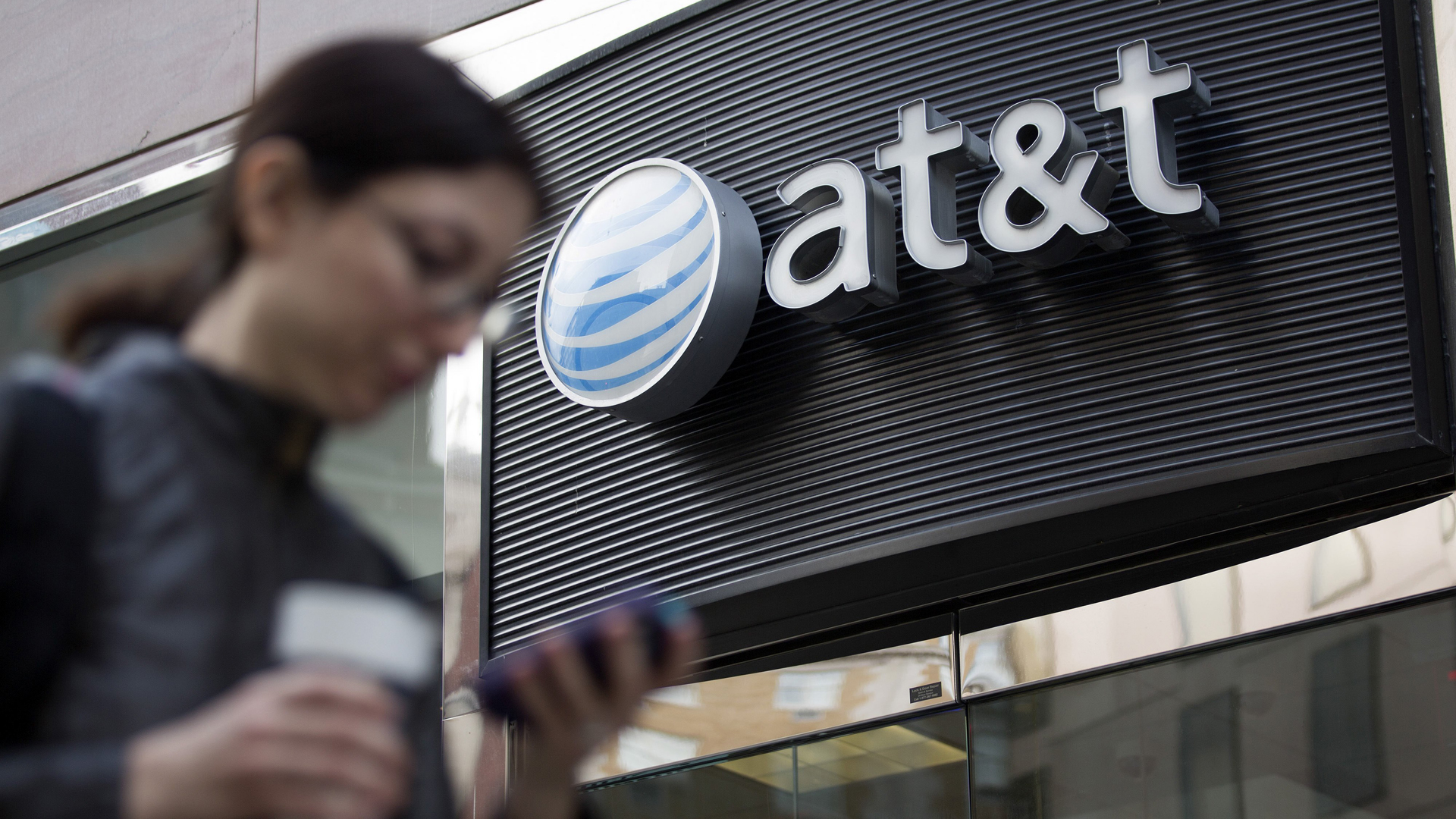 A woman checks her cellphone while walking past an AT&T store in this undated file photo. (Credit: Andrew Harper/Bloomberg/Getty Images)