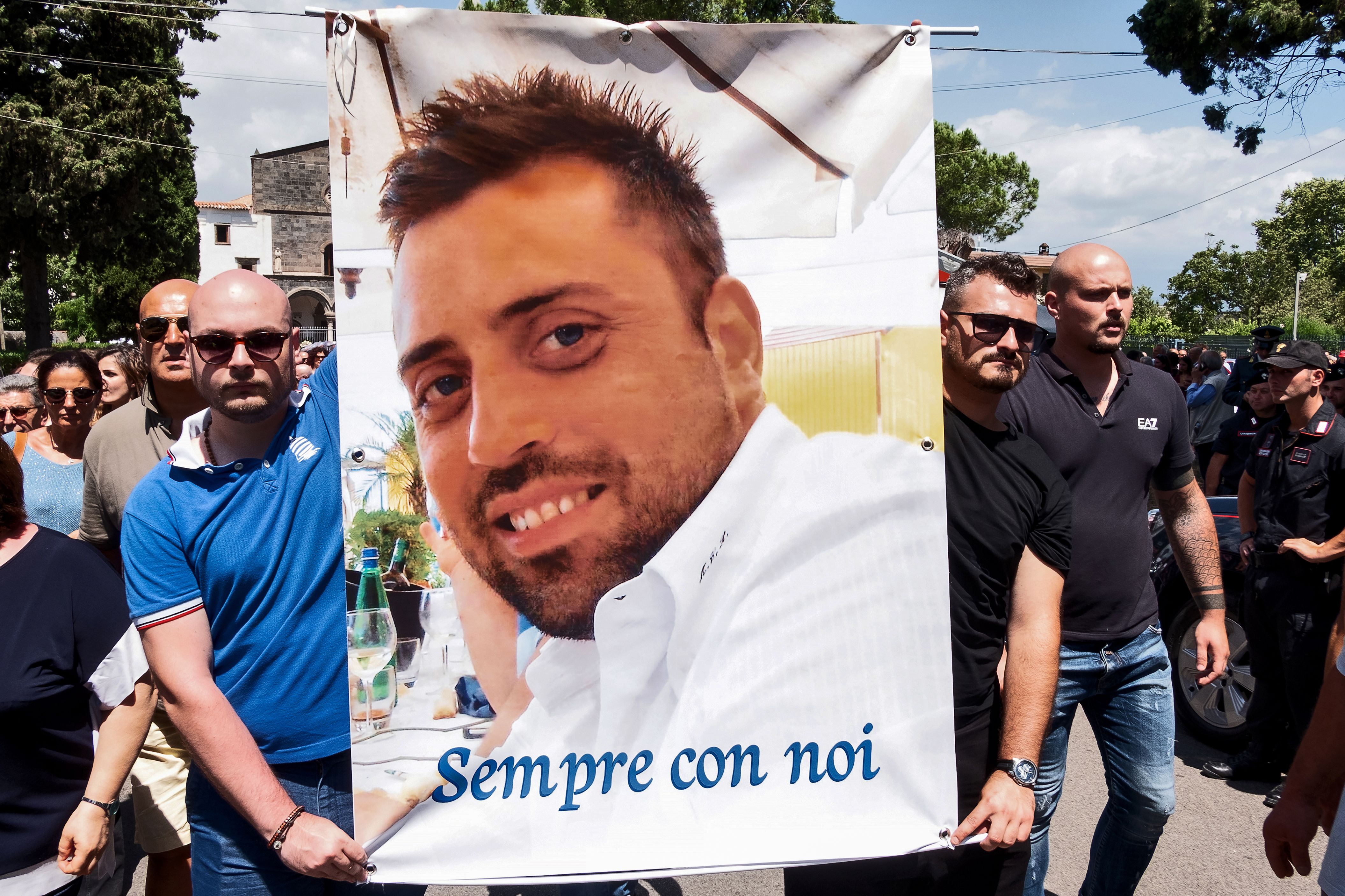 People carry a banner bearing the photo of Carabinieri officer Mario Cerciello Rega and reading "Sempre con noi" ("ever with us") at the end of the funeral mass at Santa Croce church in Somma Vesuviana, near Naples, on July 29, 2019. (Credit: ELIANO IMPERATO/AFP/Getty Images)