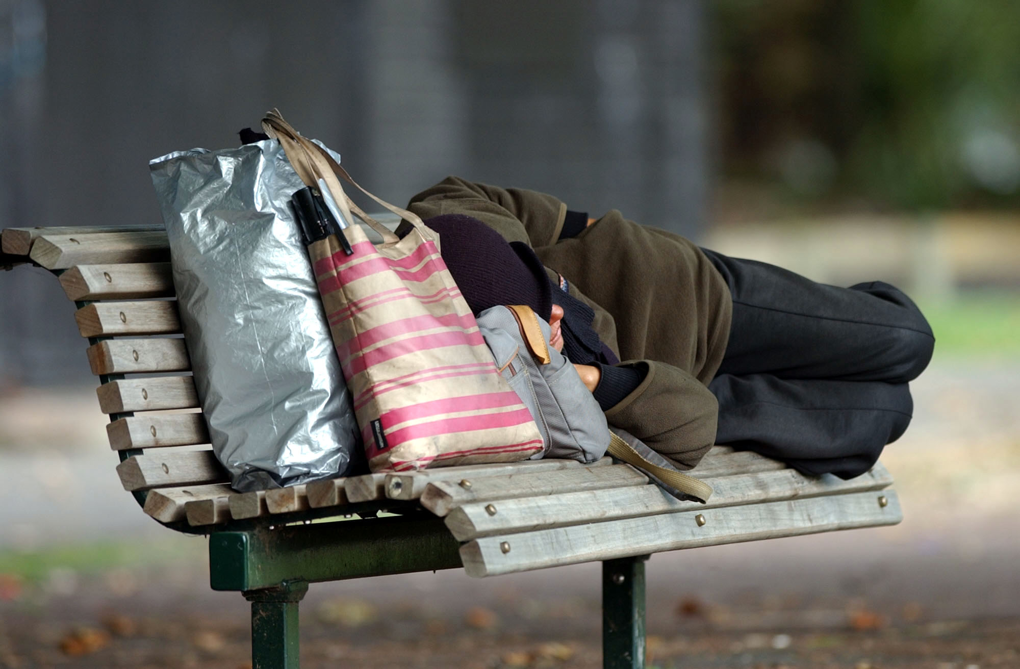 A homeless person sleeping on a park bench. (Credit: Dean Purcell/Getty Images)