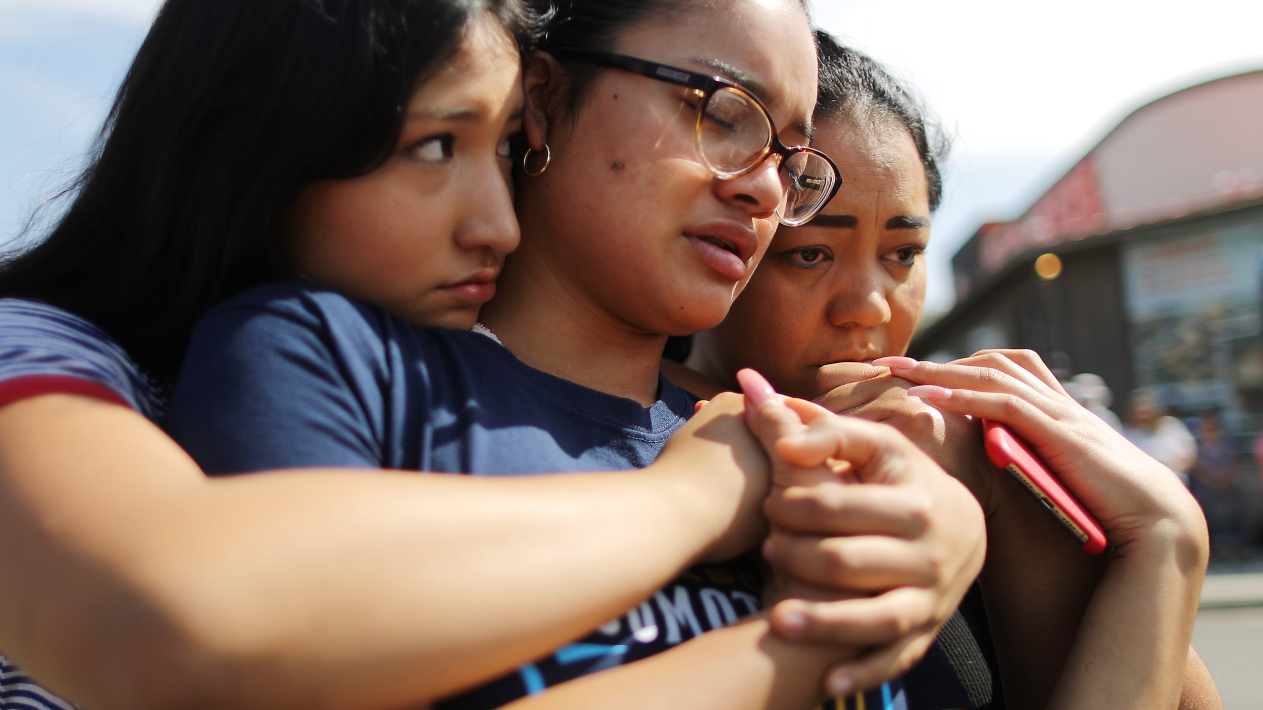 Mother Aidee Gutierrez, right, originally from Mexico, and daughters Marlene Gutierrez and Brissa Martinez embrace at a makeshift memorial outside Walmart in El Paso, near the scene of a mass shooting that days before left at least 22 people dead, on Aug. 5, 2019. (Credit: Mario Tama / Getty Images)