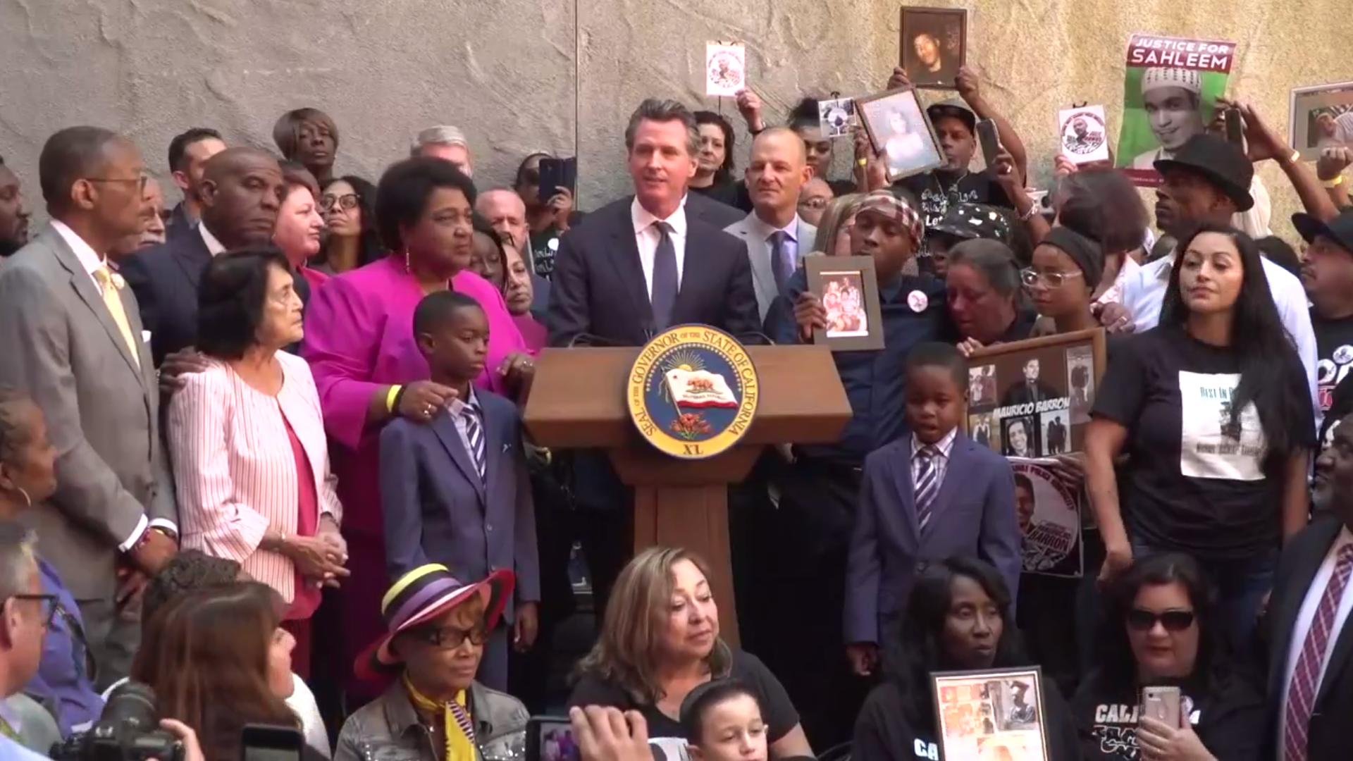 Gov. Gavin Newsom is surrounded by those who've lost family members to police shootings as he signs AB 392 on Aug. 19, 2019, in a still from a livestream shared by state Sen. Toni Atkins.